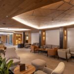 Modern hotel lobby with elegant wooden ceiling, cozy seating, and warm lighting.