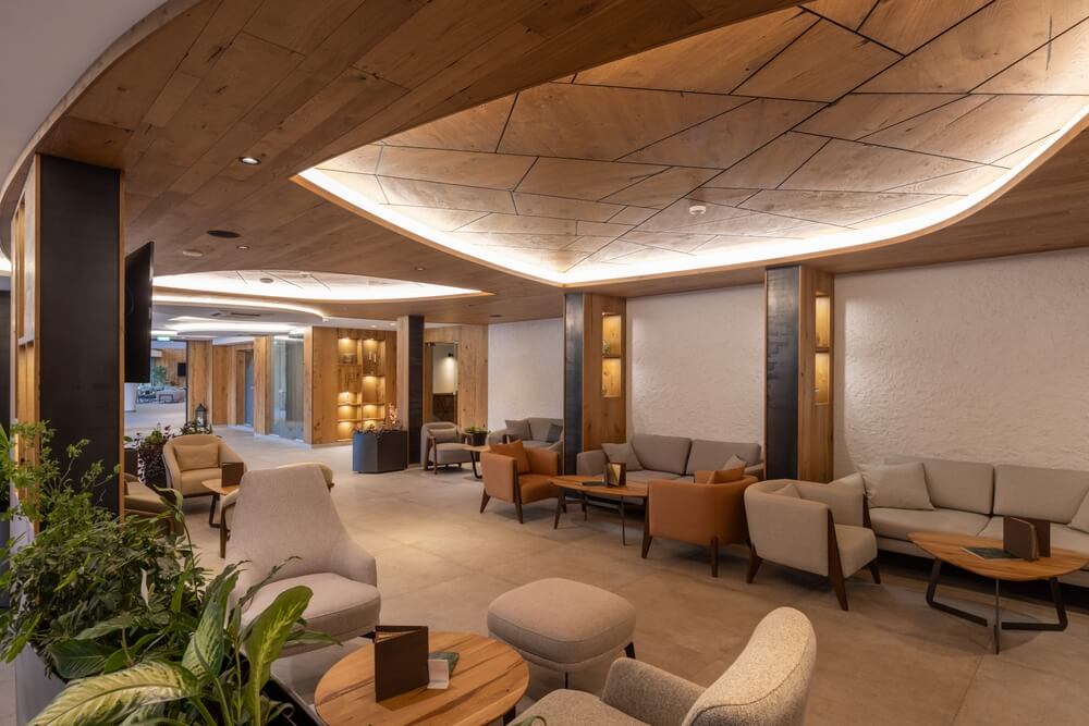 Modern hotel lobby with elegant wooden ceiling, cozy seating, and warm lighting.