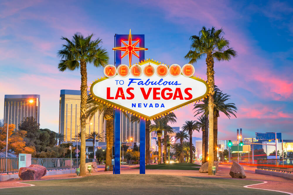 The iconic neon "Welcome to Fabulous Las Vegas Nevada" sign stands illuminated at dusk, with palm trees and a cityscape of tall buildings in the background—an emblem of a city where reliable pest control ensures the skyline remains as pristine as the clear Nevada sky.